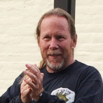 Bruce smiling and clasping his hands giving a demonstration